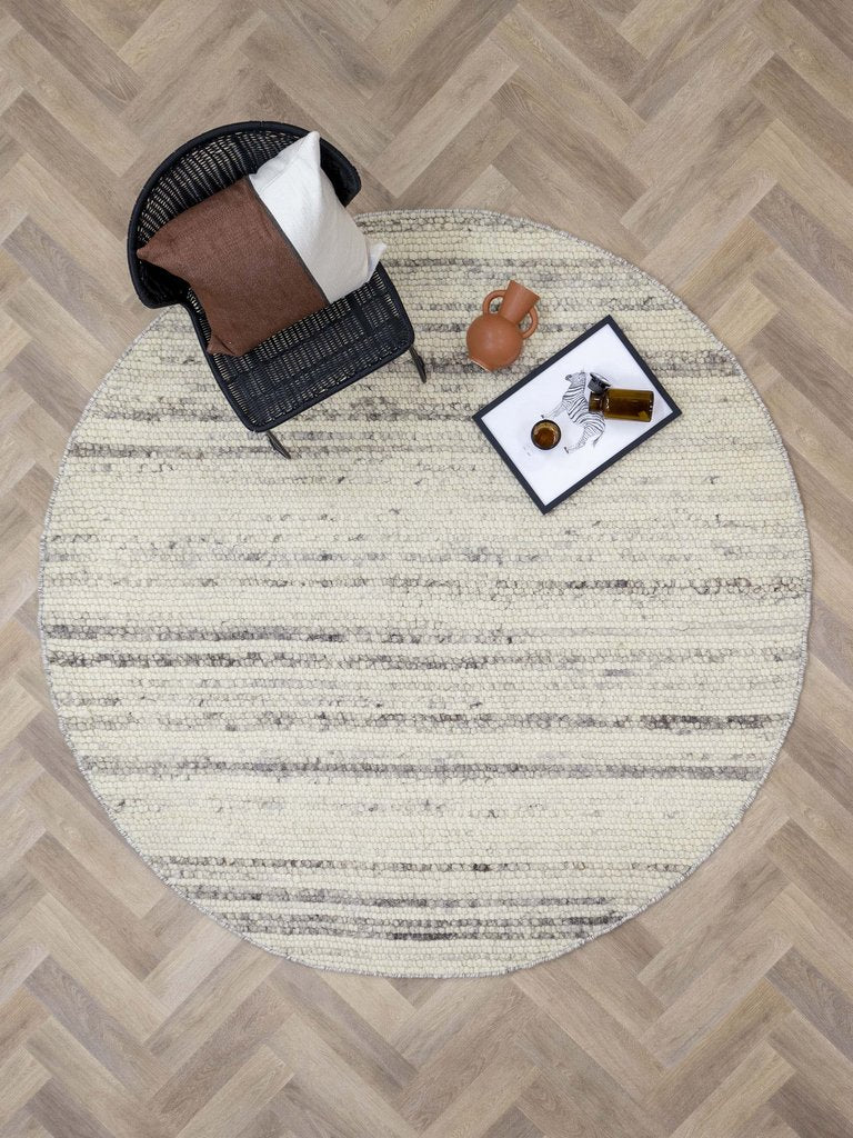 Rond beige vloerkleed met grijze accenten onder een zwarte fauteuil